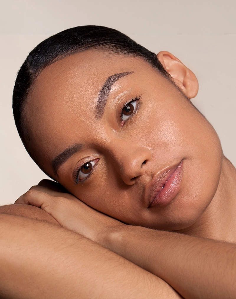 A vertical close-up of a woman with clear, radiant skin resting her head on her arm. She is looking into the camera with a soft, neutral expression. - Laser Resurfacing for Scars in California.